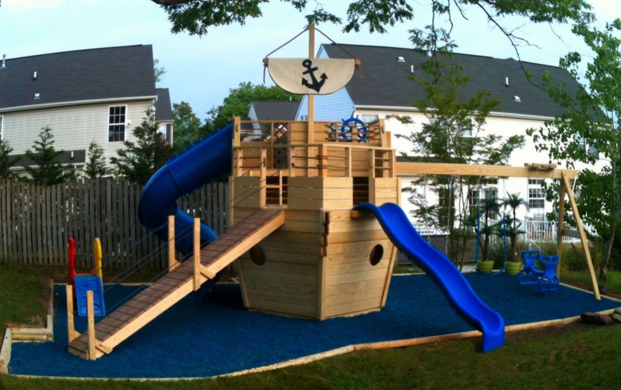 Custom wooden home playset with blue slides on blue rubber mulch in a residential backyard