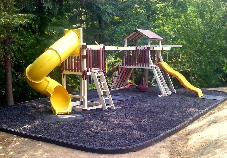 Wooden backyard playset with a yellow tube slide on brown rubber mulch