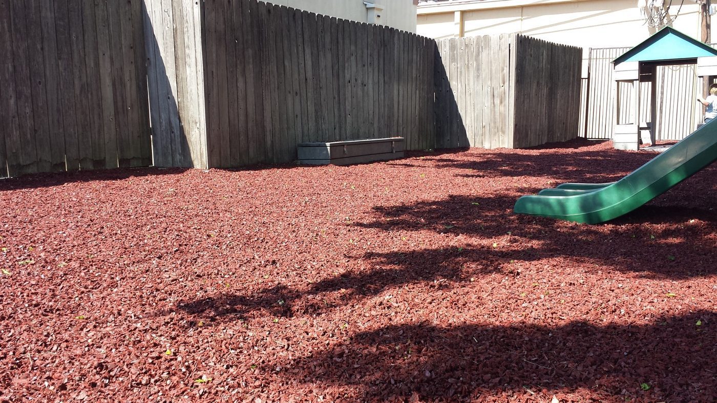 HOA community playground with a tan tube slide on black rubber mulch safety surfacing