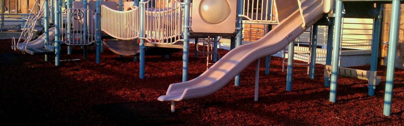 A community-park playground on a red rubber mulch fall surface