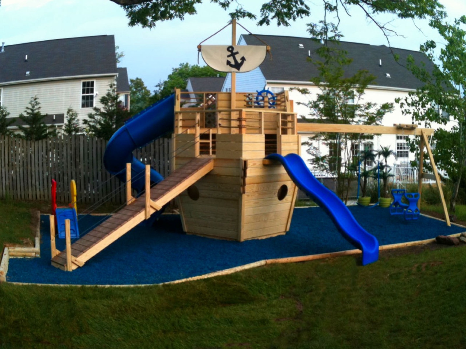 Wooden pirate-ship playset with a slide on a rubber mulch surface