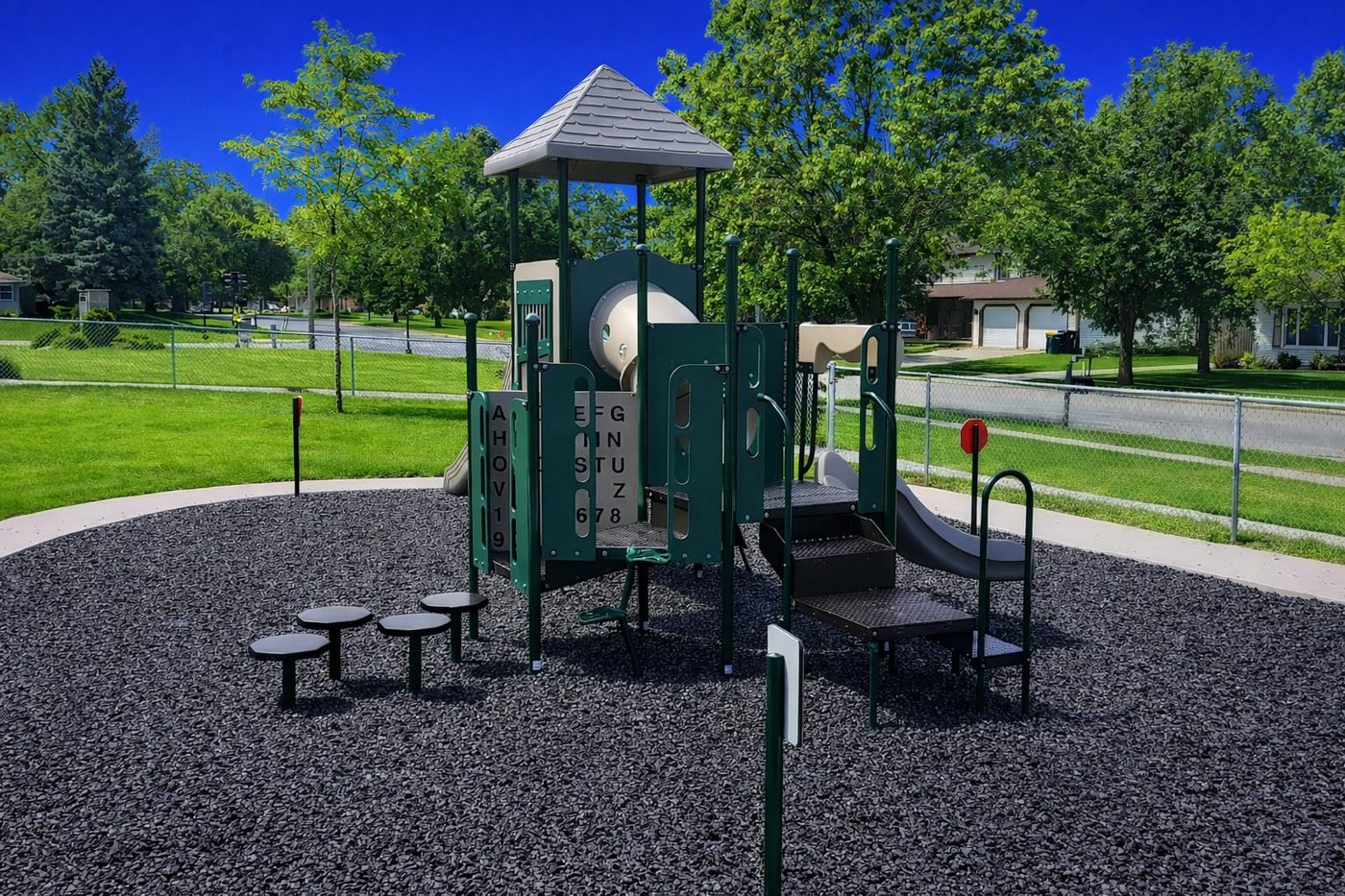 Park play structure beside picnic tables on a rubber mulch surface