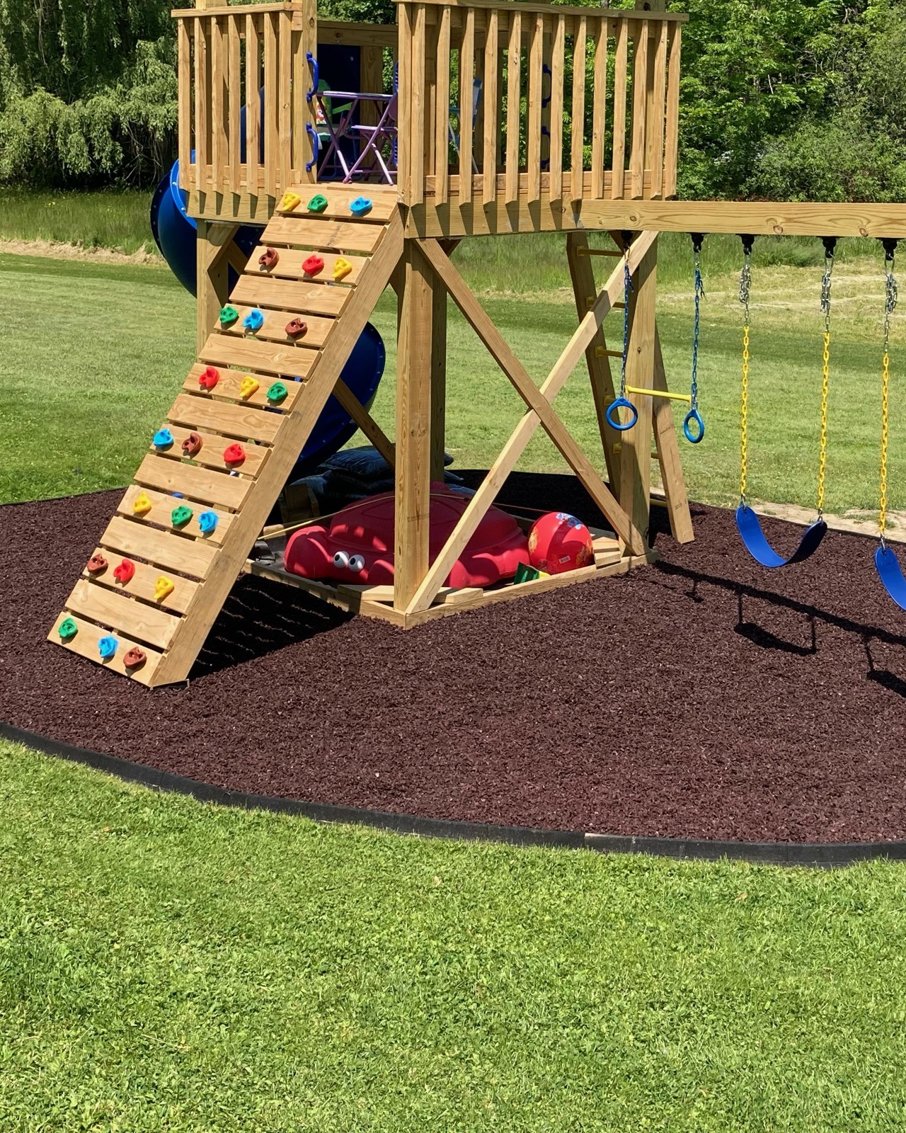 Wooden backyard playset with a climbing wall on rubber mulch