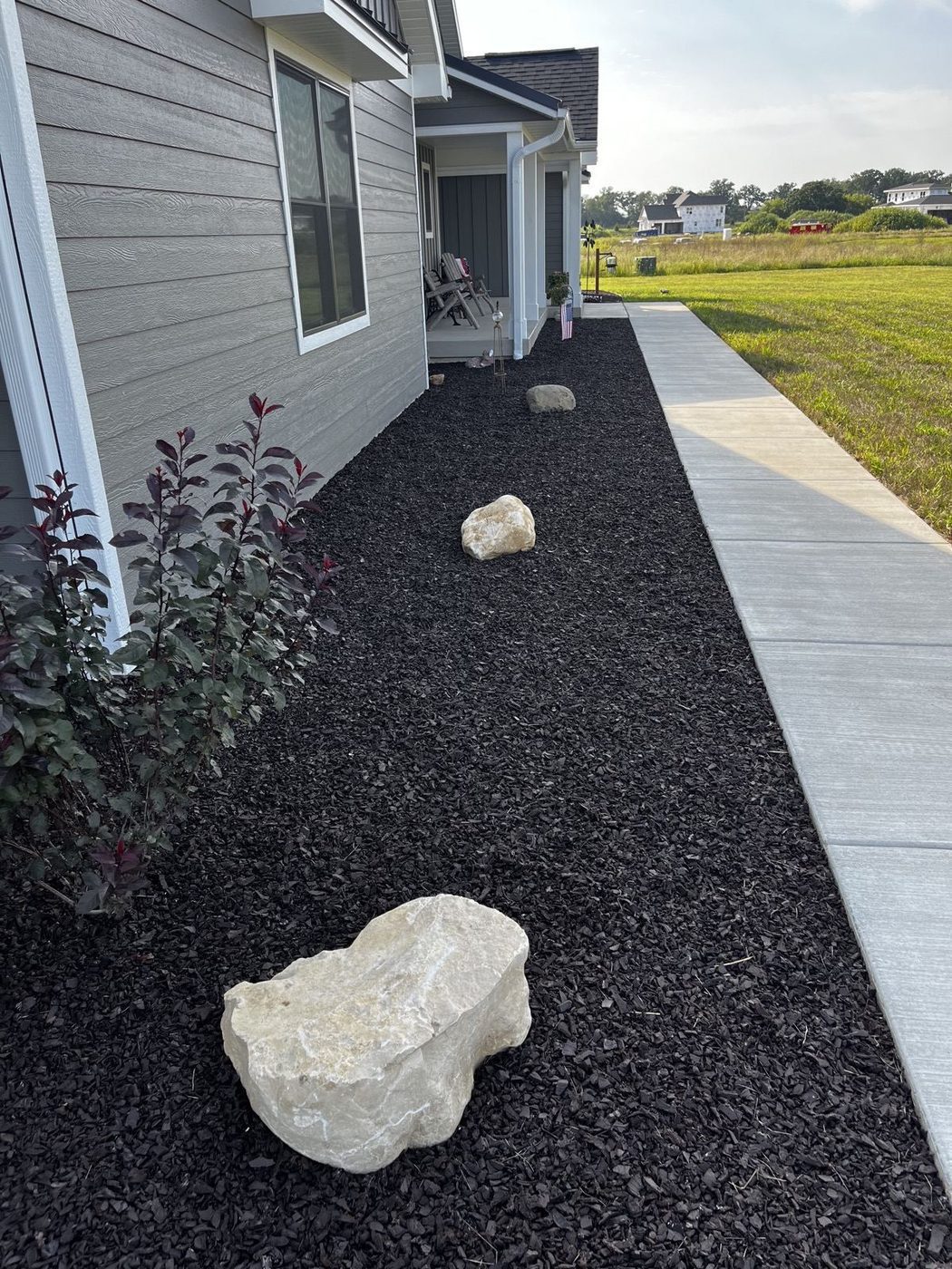 Black rubber mulch garden bed with accent boulders along a walkway