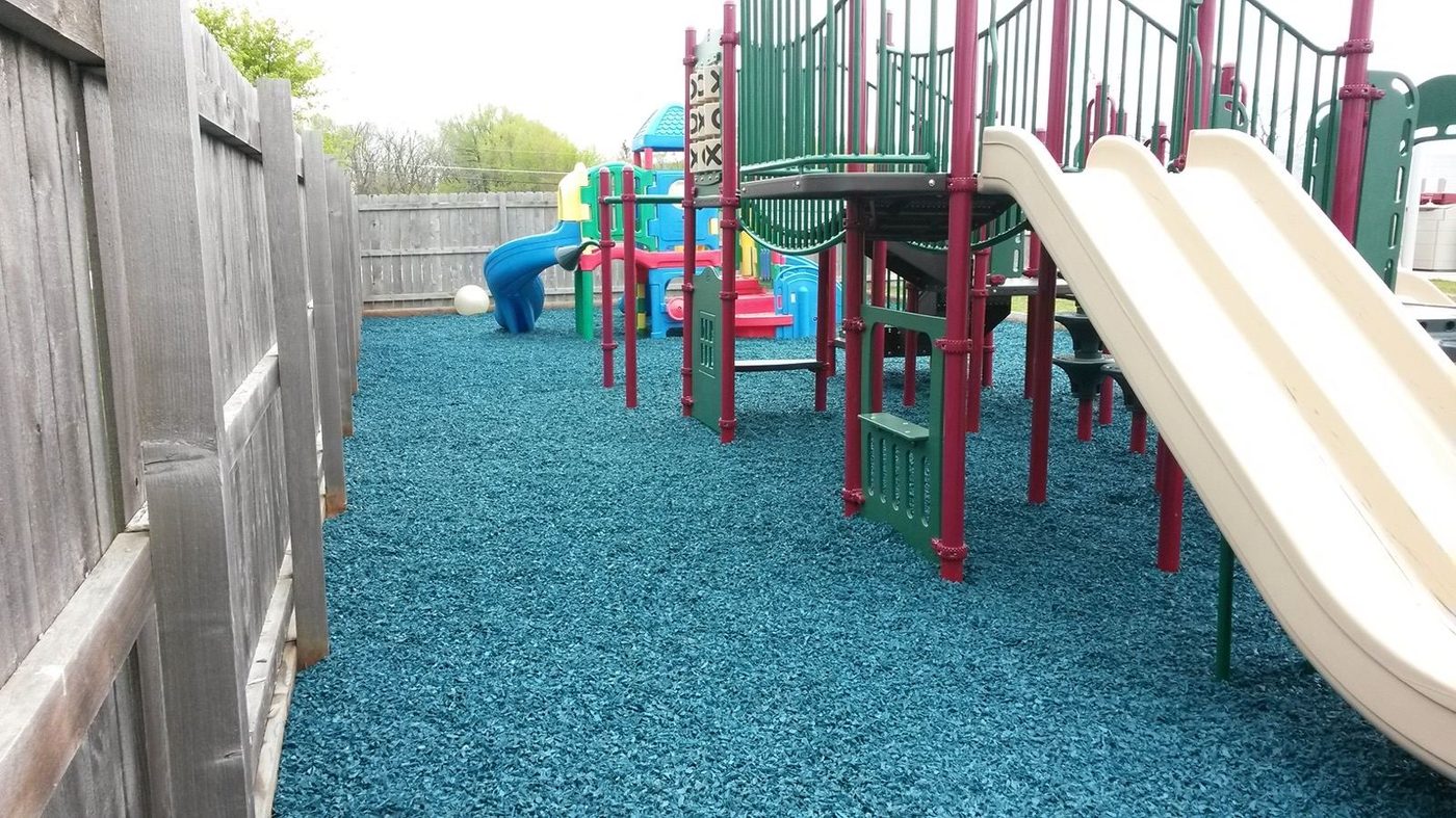 Fenced daycare play area with a slide on rubber mulch