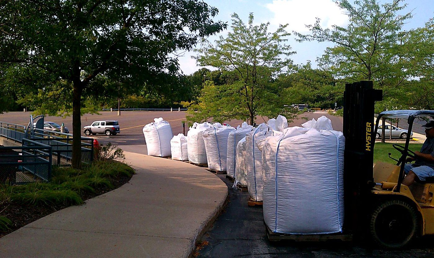 Super sacks of rubber mulch lined up on pallets after a box-truck delivery, a forklift setting them in place