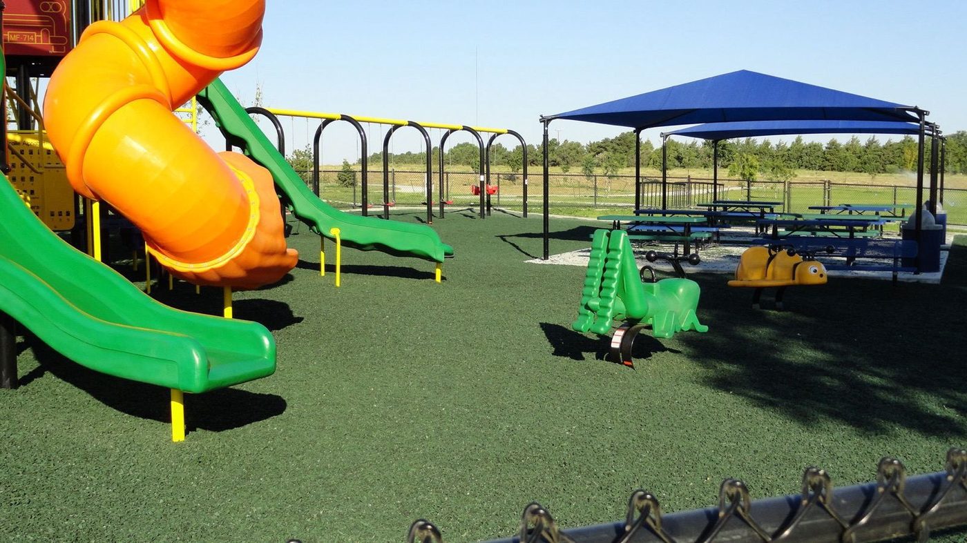 Green rubber mulch at a city park playground with a shade pavilion